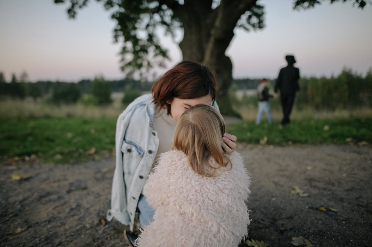A tender moment between mother and daughter outdoors in a grassy field at twilight.
